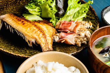 Grilled Atka mackerel set meal with rice, miso soup and salad against a blue plaster design board. 