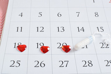 Close-up of a calendar with red hearts and a tampon. The concept of Pms and women's critical days