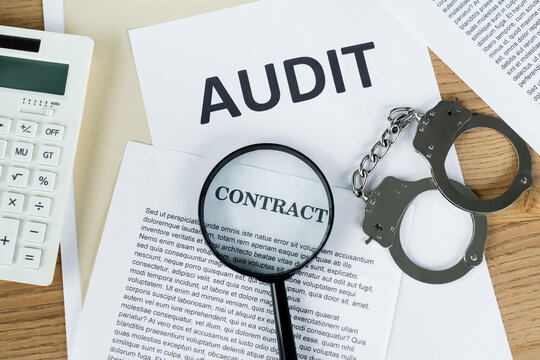 top view of magnifier on papers with audit and contract lettering near calculator and handcuffs.
