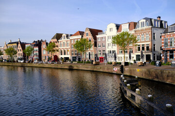 Fototapeta na wymiar Haarlem, Netherlands - April 12. 2022: Traditional Dutch houses lining the river Sparne viewed from the Melkbrug bridge in springtime.