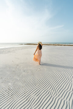 young hispanic woman with dress and hat on a beach with textured sand