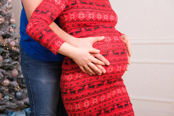 Husband hugs pregnant wife and pats on the belly, pregnancy for Christmas, close-up, copy space