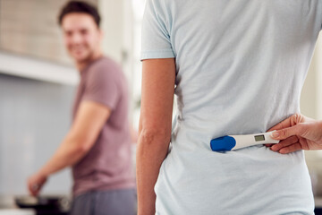 Transgender Couple At Home In Kitchen With Woman Surprising Man With Positive Pregnancy Test