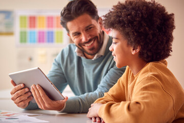 Teacher And Male Student In School Classroom Using Digital Tablet Together