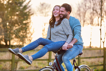 Couple Riding Bike Through Countryside With Woman Sitting On Handlebars