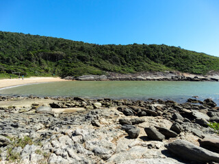 Linda praia com grandes pedras, banhado pelas ondas do mar, com céu azul e linda paisagem ao fundo...