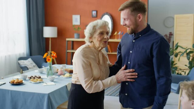 Joyous senior grandmother smiling and hugging family members while greeting them at home before holiday dinner
