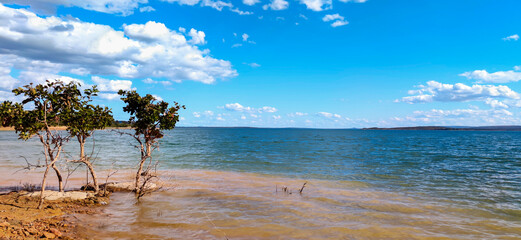 Linda vista de parte da represa de três marias, com água límpida, céu azul com nuvens e pequenas árvores na beirada, na região de Três Marias, Minas Gerais, Brasil.