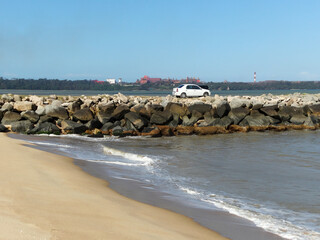 Lindo Mirante feito com grandes pedras, um carro branco em cima, banhado pelas ondas do mar, com c&eacute;u azul e grandes navios ao fundo fotografado em Vit&oacute;ria no estado do Esp&iacute;rito Santo, Brasil.