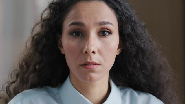 Close up serious female face beautiful woman with natural makeup perfect skin arabian young girl student businesswoman with curly hairstyle wears formal shirt looking at camera with questioning look