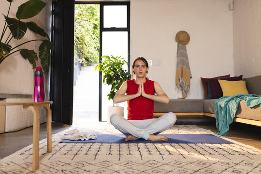 Non-binary trans woman practicing yoga and meditation sitting on yoga mat at home