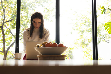 Thoughtful non-binary trans woman using laptop in the kitchen at home