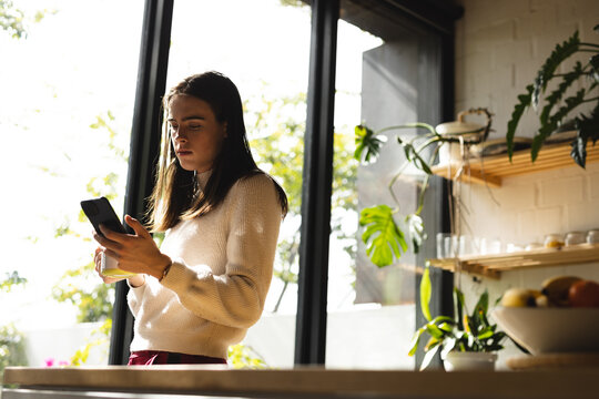 Thoughtful non-binary trans woman using smartphone near the window at home