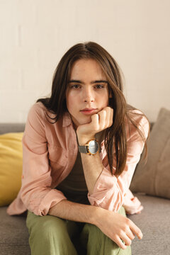 Portrait of thoughtful non-binary trans woman with hand on chin sitting on the couch at home