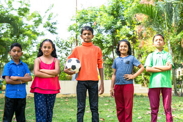 team of kids with football standing confidently by looking camera at park - concept of champions, aspirations and leisure activities