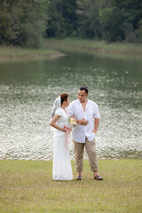 The bride and groom are taking pictures in the beautiful natural forest wearing white dresses.