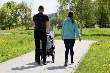 Couple walking with baby pram in summer park. Young parents, leisure on nature