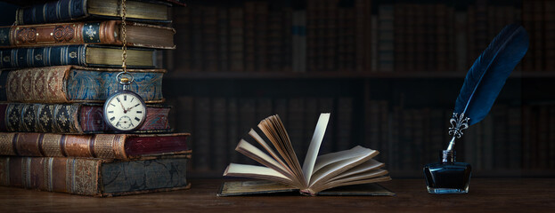 Old clock on background of old books an open book and a fountain pen in an inkwell. Сlock as a...