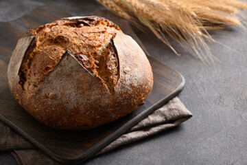 Loaf of freshly baked whole grain bread and barley spikelet on brown background. Close up. Copy space.