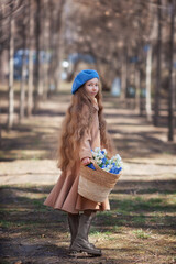 Little pretty girl kid walks through the forest in spring and collects the first flowers in basket .