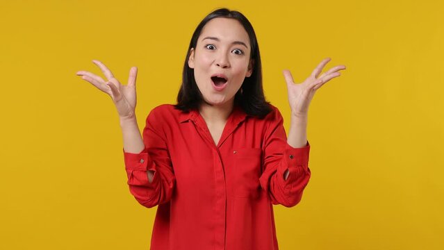 Shocked amazed young woman of Asian ethnicity 20s wear red shirt look camera say wow doing mind exprosion gesture isolated on plain yellow background studio portrait. People emotions lifestyle concept