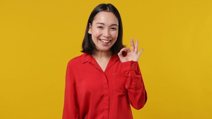 Smiling cheerful young woman of Asian ethnicity 20s years old wear red shirt showing okay ok zero fingers gesture isolated on plain yellow background studio portrait. People emotions lifestyle concept