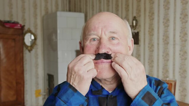 Seniour Caucasian man putting on false moustache looking at the camera enjoying and smiling, cozy warm slowmo. High quality 4k footage