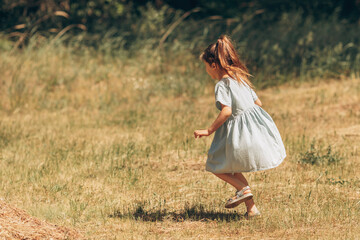 A little schoolgirl girl runs and jumps in the meadow on a summer sunny day, a child in a denim light dress