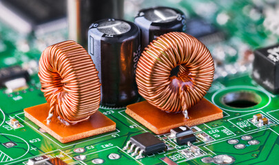 Closeup of toroidal inductors and electrolytic capacitors on electronic PCB detail with bokeh. Two ferrite core coils with copper wire winding and various surface-mount devices on green circuit board. - obrazy, fototapety, plakaty