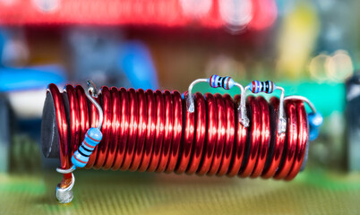 Electronic coil with ferrite core and blue small color coded resistors on red copper wire. Cylindric electromagnetic inductor on PCB detail of cable TV amplifier with colored bokeh in blur background. - obrazy, fototapety, plakaty