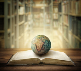 Old globe lying on an open book against the background of bookshelves in a library. Selective...