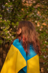 Yellow and blue fabric on the girl. Teen girl is standing with the Ukrainian flag.