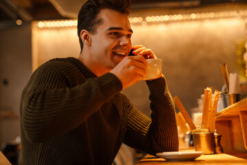 Young white man using cellphone and drinking coffee in cafe