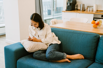 Young cute asian girl with phone chatting sitting on couch