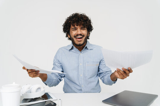 Displeased indian man is holding papers and sitting by table