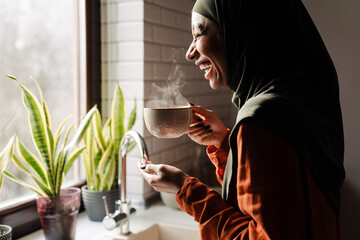 Young laughing woman in hijab holding cup of hot tea