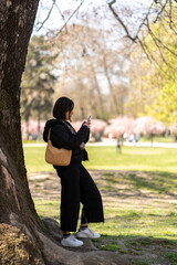 Stylish woman standing near the tree while using smartphone