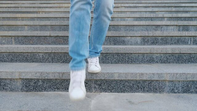 A teenage girl in white sneakers and jeans going down the concrete stairs. Close view of the legs