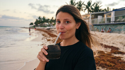 Fototapeta na wymiar latina girl drinking Argentinian traditional drink called mate in the beach