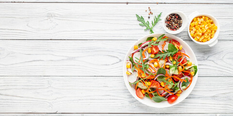 Fresh salad with vegetables. Arugula, spinach, cucumbers, tomato, onions carrots, corn andradishes in a plate on the table. Diet nutrition. Top view. Copy space