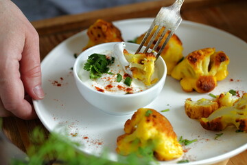 Women's hands with a knife and fork.Cauliflower in batter with white spicy sauce