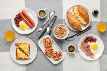Hearty homemade family breakfast. Eggs, bacon, sausages, beans, croissants, toast and coffee on the table. Top View