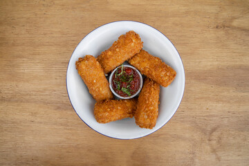 Gastronomy. Rustic presentation. Top view of fried mozzarella cheese fingers with a spicy dipping sauce, in a white bowl on the wooden table. 