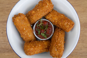 Gastronomy. Rustic presentation. Top view of fried mozzarella cheese fingers with a spicy dipping sauce, in a white bowl on the wooden table. 