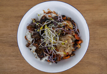 Vegan cuisine. Gluten free. Top view of a bowl with grilled tofu, soy sprouts, pumpkin seeds, season vegetables, spicy mango, sushi rice, cucumber and kimchi, in the restaurant wooden table.