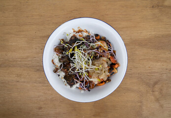 Vegan cuisine. Gluten free. Top view of a bowl with grilled tofu, soy sprouts, pumpkin seeds, season vegetables, spicy mango, sushi rice, cucumber and kimchi, in the restaurant wooden table. 