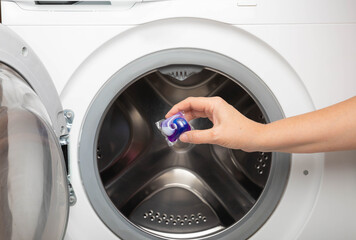 A woman put a liquid powder capsule into a washing machine with laundry, close-up. Gel for washing...