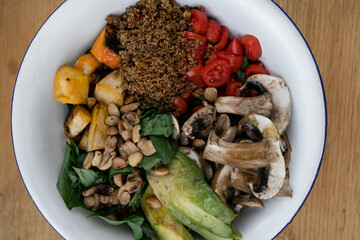 Vegan cuisine. Top view of a fresh salad, with sliced avocado, grilled pumpkin, quinoa, mushrooms, cherry tomatoes and roasted chestnuts, in a white bowl on the wooden table.
