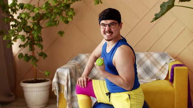 Indoors portrait of man in bright sport clothes exercising with small dumbbells at home,slow motion. Funny Sport activity.