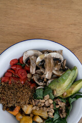 Vegan cuisine. Top view of a fresh salad, with sliced avocado, grilled pumpkin, quinoa, mushrooms, cherry tomatoes and roasted chestnuts, in a white bowl on the wooden table.